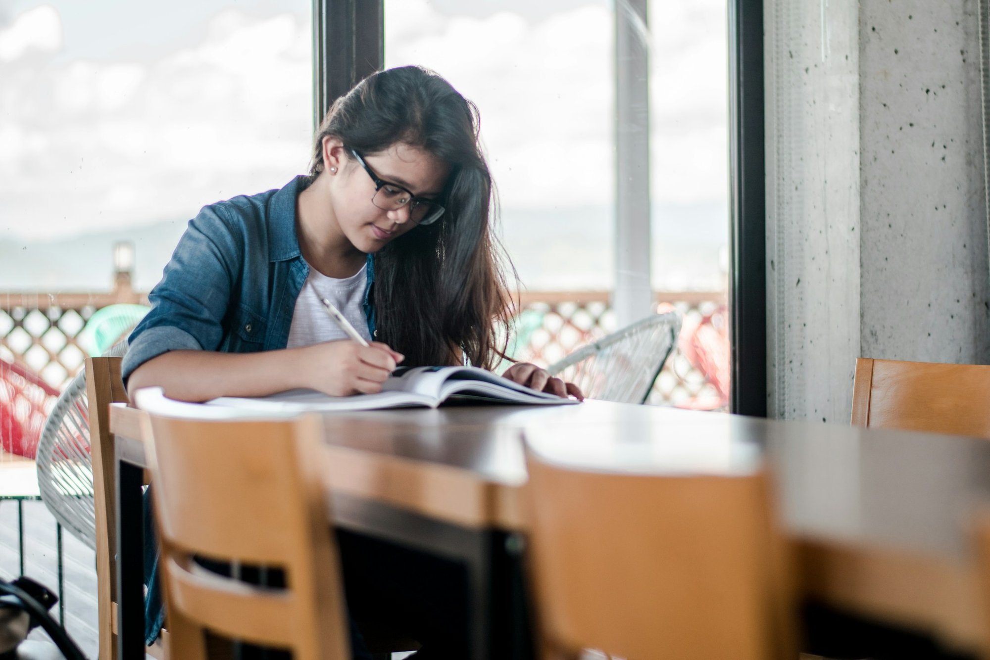 A student working through a textbook at a table by the window