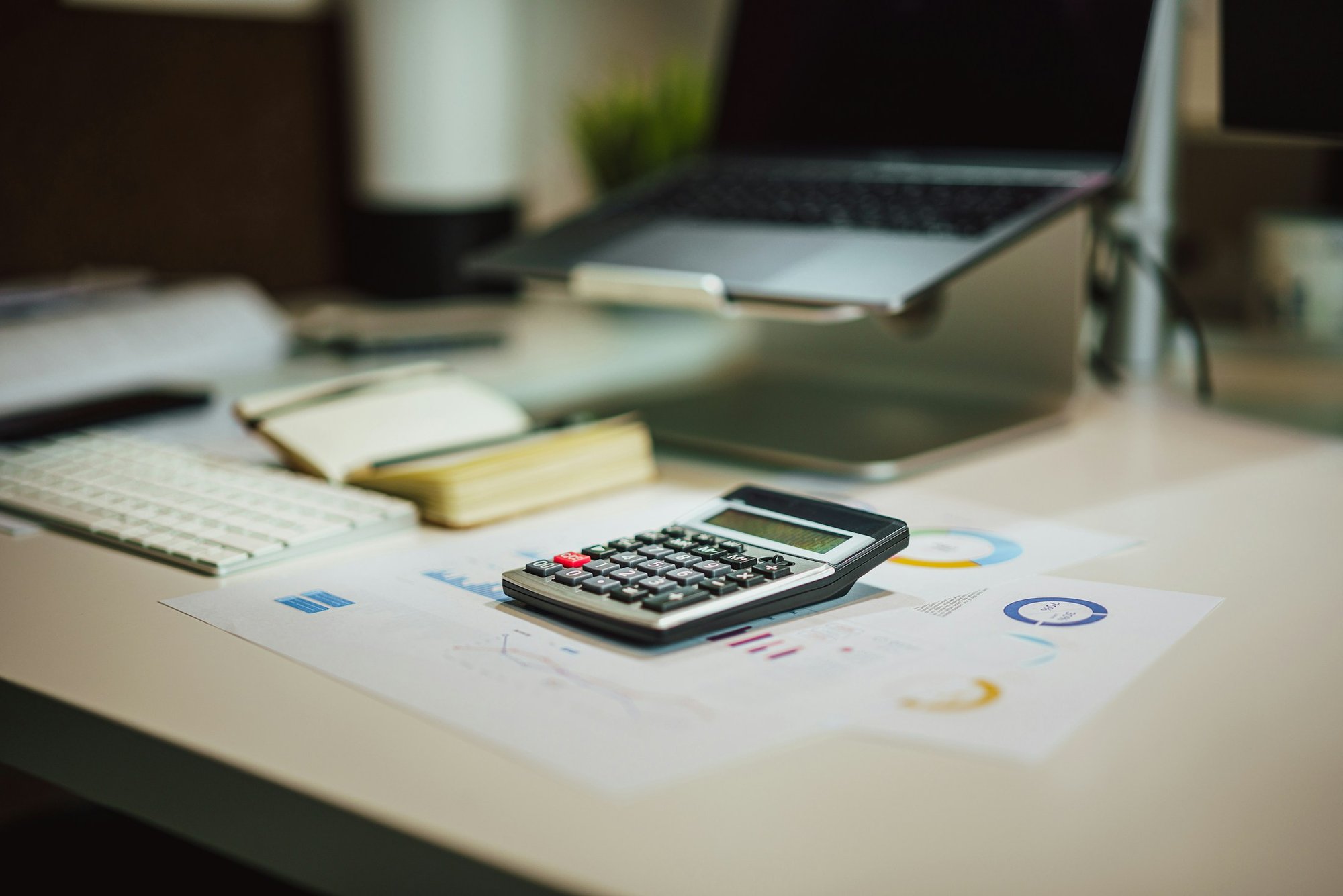 A calculator and notebook on a desk beside a laptop