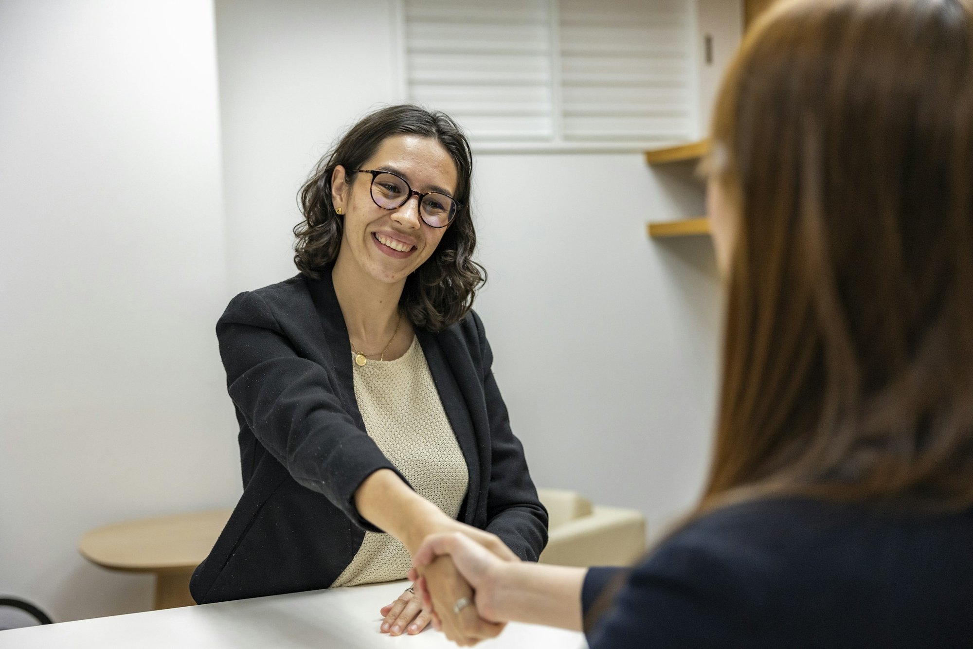 Two people shaking hands across a desk after a meeting