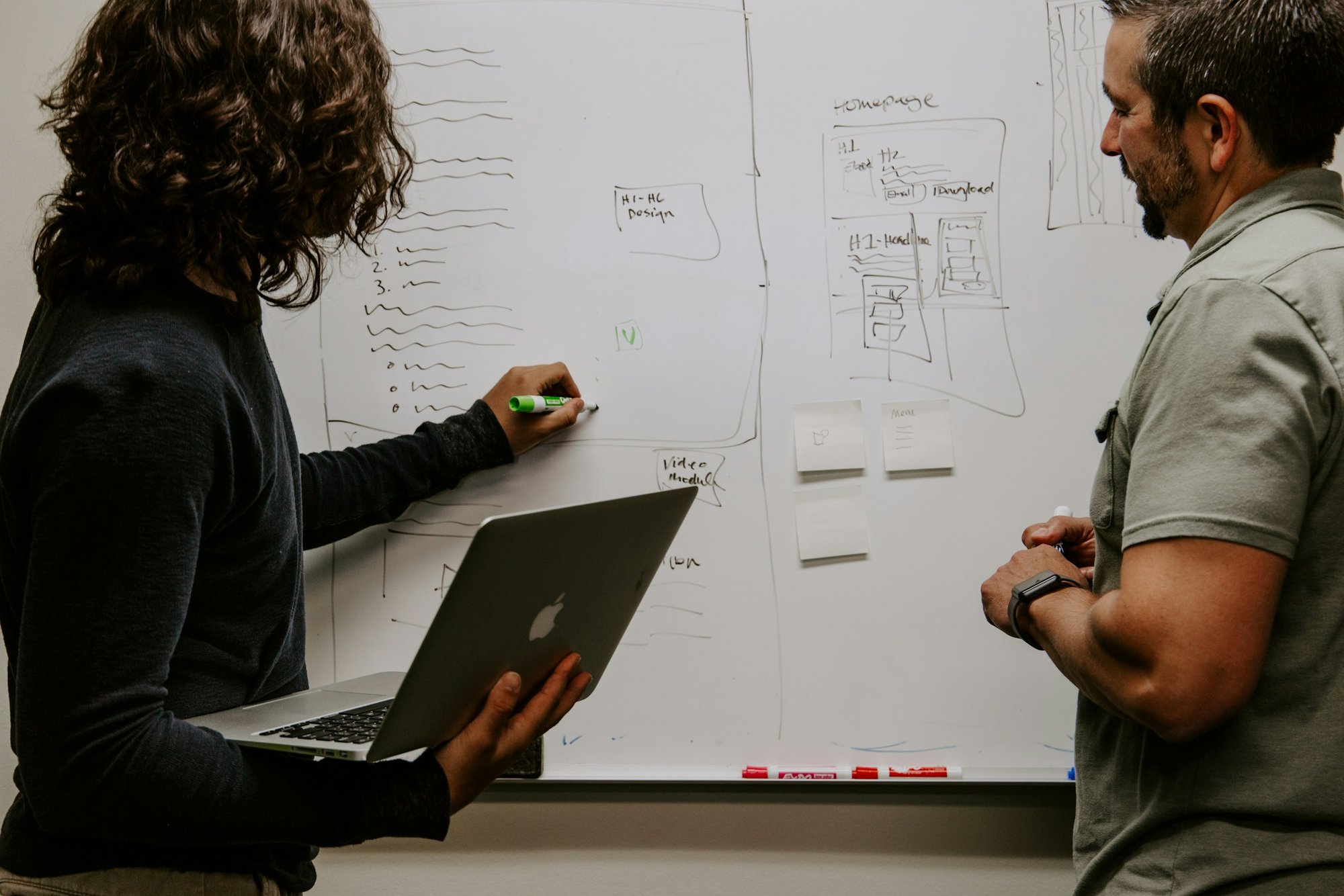 Two engineers discussing a diagram on a whiteboard