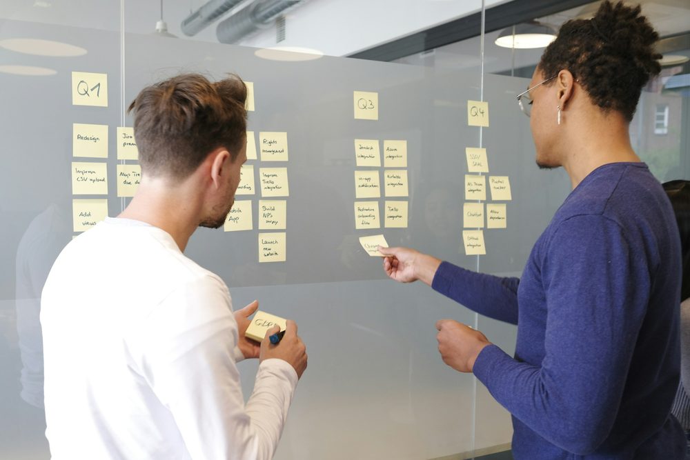 Two colleagues planning work on a wall of sticky notes
